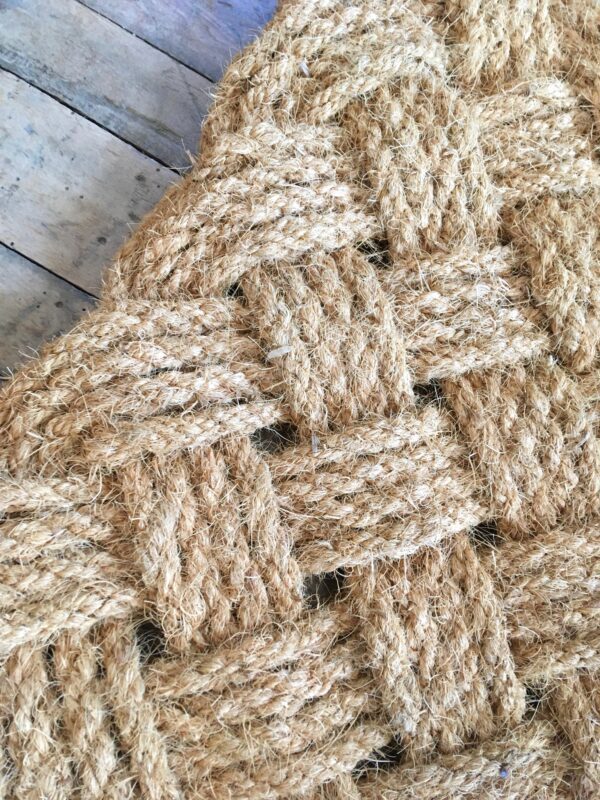 A light-colored sturdy doormat made of woven rope.