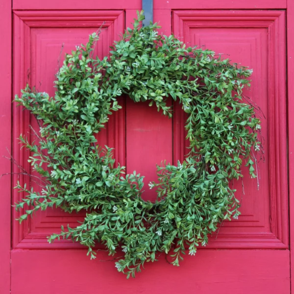 Realistic artificial boxwood wreath in a spiral shape hanging on a red door