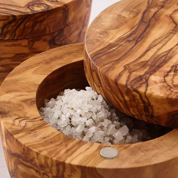 Closeup image of round olive wood salt cellar open to show salt.