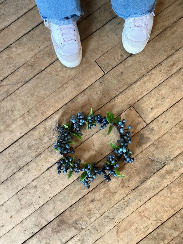 A naturalistic artificial wreath, approximately 11 inches in diameter with a woven twig frame and realistic blueberries and and blueberry leaves.