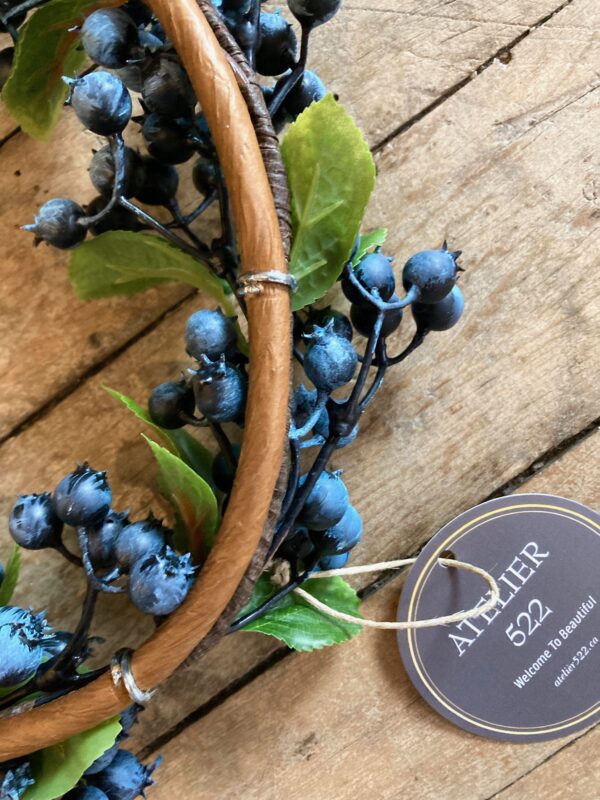 A naturalistic artificial wreath, approximately 11 inches in diameter with a woven twig frame and realistic blueberries and and blueberry leaves.