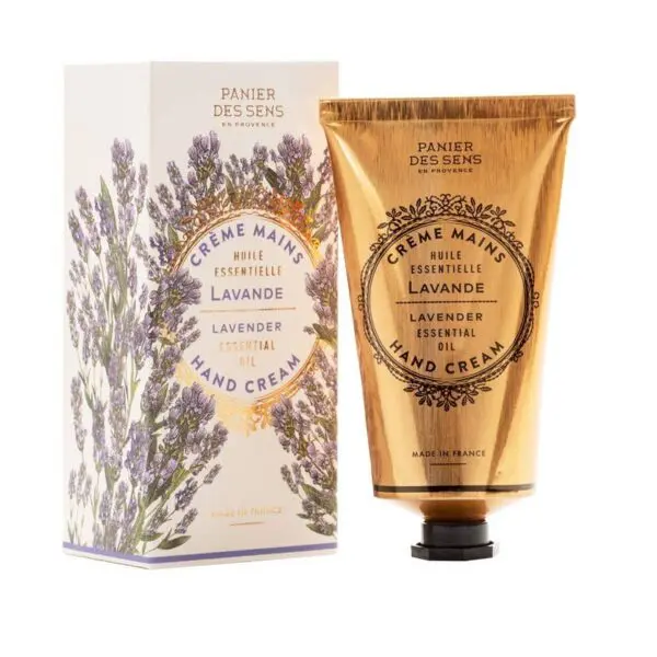 A gold-colored tube of hand cream is displayed alongside its decorative box. The tube features a black cap and is labeled "Crème Mains" with "Lavande" and "Lavender Essential Oil" prominently featured. The box is adorned with illustrations of lavender flowers in shades of purple and green, enhancing its elegant appearance. Both items are branded with "Panier des Sens" and indicate they are made in France.