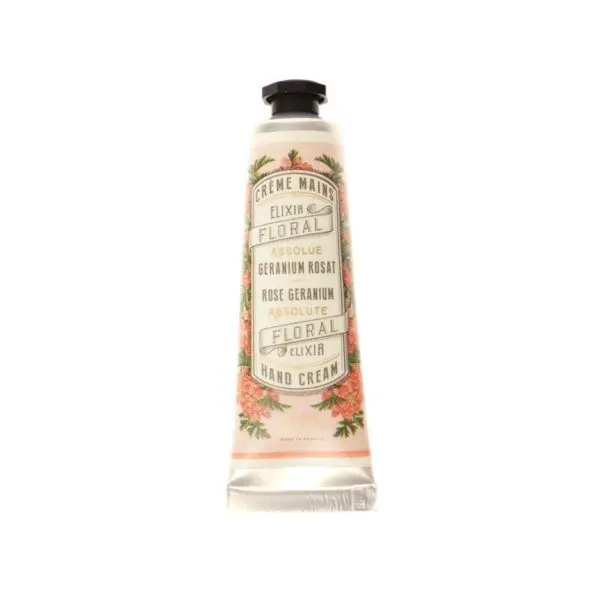 A metal tube of hand cream with a floral design. The label features the text "Crème Mains," "Floral Elixir," and "Hand Cream," along with mentions of "Geranium Rosat" and "Rose Geranium Absolute." The background is a soft pink with decorative floral elements, and the tube has a black cap.