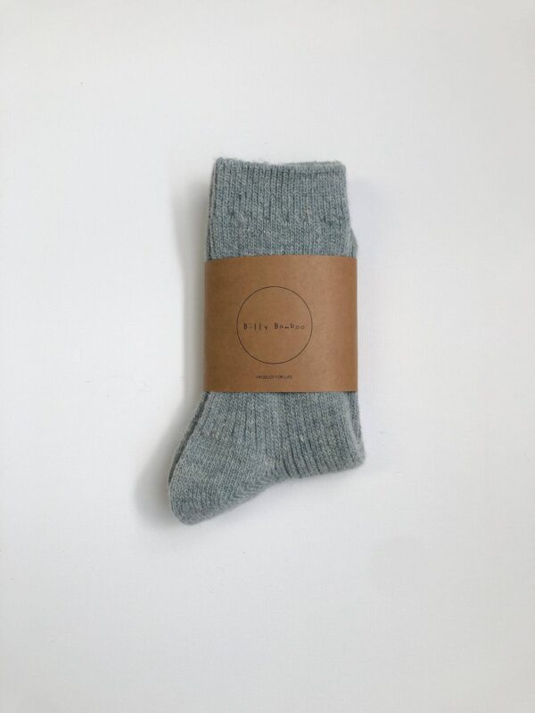 A single pair of light gray socks is neatly folded and secured with a brown paper band. The band features a circular logo with the text "Billy Bamboo" and the phrase "PRODUCT FOR LIFE." The socks have a ribbed texture at the top and a smooth finish on the body. The background is plain white, emphasizing the socks and packaging.