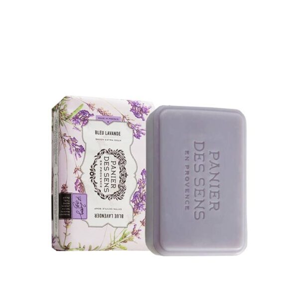 A rectangular bar of lavender soap is displayed next to its decorative packaging. The soap is a soft purple color and features the embossed text "PANIER DES SENS EN PROVENCE." The box is adorned with floral illustrations, primarily in shades of purple and green, and includes the label "BLEU LAVANDE" along with details about the product being an extra gentle soap. The overall aesthetic conveys a natural and soothing vibe, typical of lavender products.