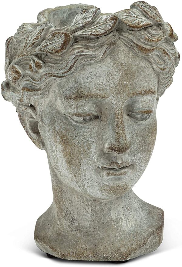 A decorative planter shaped like a human head, featuring a smooth, pale gray finish. The head has a serene expression with closed eyes and slightly parted lips. It is adorned with a crown of leaves, adding a natural element to the design. The base is rounded and sturdy, suitable for holding plants or flowers. The overall style suggests a classical or artistic influence.