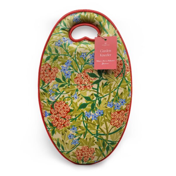 A garden kneeler with a vibrant floral design featuring red and blue flowers against a green background. The kneeler has a rounded shape with a handle at the top for easy carrying. It is bordered in red and includes a tag that reads "Garden Kneeler" along with details about the William Morris Collection.