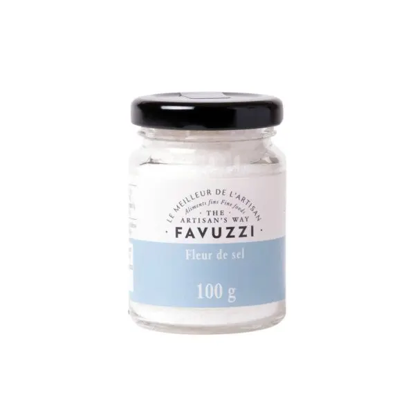 A small glass jar with a black lid contains Fleur de Sel salt. The jar is labeled with the brand name "Favuzzi" and features a light blue band indicating the weight of 100 grams. The design is simple and elegant, emphasizing the artisanal quality of the product.