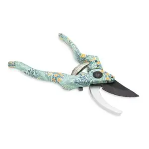 A pair of pruning shears with a decorative floral pattern on the handles. The handles are predominantly light blue with green leaves and small orange flowers. The shears feature a curved blade made of metal, with one side being serrated and the other smooth. A spring mechanism is visible between the handles, and there is a black button on one side for locking or unlocking the shears. The background is plain white, emphasizing the design of the tool.