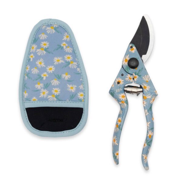 A pair of floral-patterned pruning shears is displayed alongside a matching protective sheath. The shears feature a light blue handle adorned with white daisies and green leaves, while the sheath has a similar floral design on a blue background, with a black bottom section. The shears have a sharp, curved blade and a locking mechanism for safety.