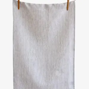 A striped fabric towel is hanging on a clothesline, secured with wooden clips. The towel features a pattern of thin, vertical stripes in light and dark shades, creating a simple yet elegant design. The background is neutral, emphasizing the towel's texture and pattern.