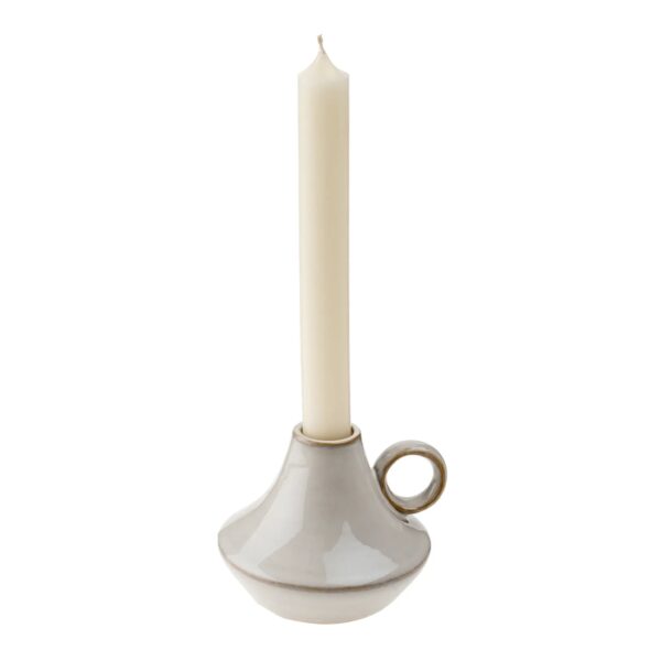 A slender, cream-colored candle stands upright in a modern, ceramic candle holder. The holder has a smooth, glossy finish and a unique shape, featuring a wide base that tapers towards the top. It includes a small handle on one side, adding to its contemporary design. The overall color scheme is neutral, emphasizing a minimalist aesthetic.