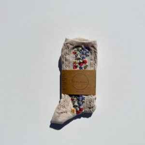 A single pair of light beige socks is displayed against a white background. The socks feature a textured knit pattern and are adorned with colorful floral embroidery in red, blue, and yellow. They are secured with a brown paper tag that includes the brand name "Billy Bamboo" and additional product information.