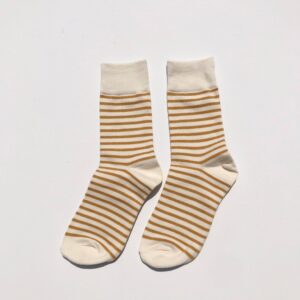A pair of socks is displayed, featuring a cream base color with alternating thin and thick stripes in a warm, golden brown. The socks have a solid cream cuff at the top and a rounded toe design. They are positioned side by side on a plain white background.